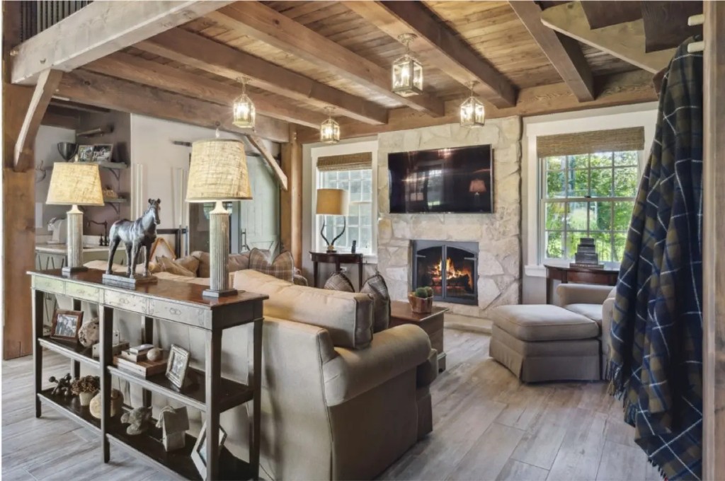 Rustic luxury living room with stone fireplace, wood beams, and neutral furnishings by Phase 4 Design Group